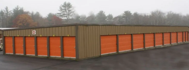 Row of tan storage buildings with orange roll-up doors at Middleboro Mini Storage